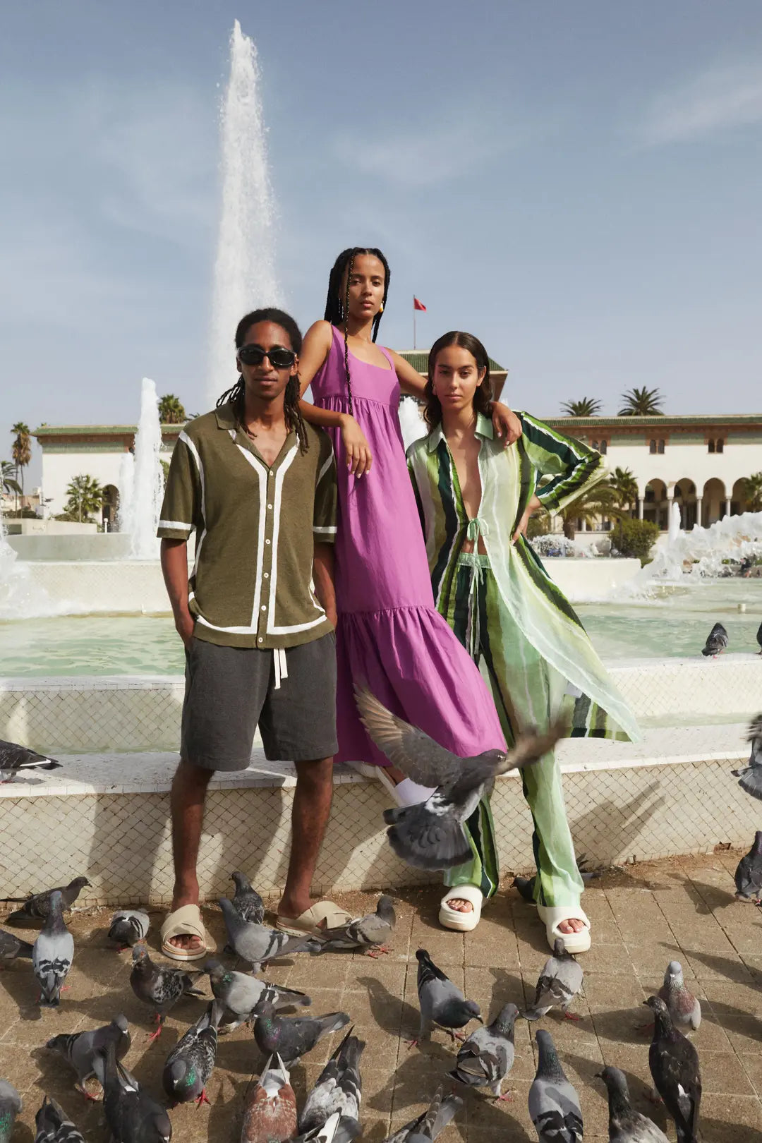 Three people standing in front of a fountain with pigeons