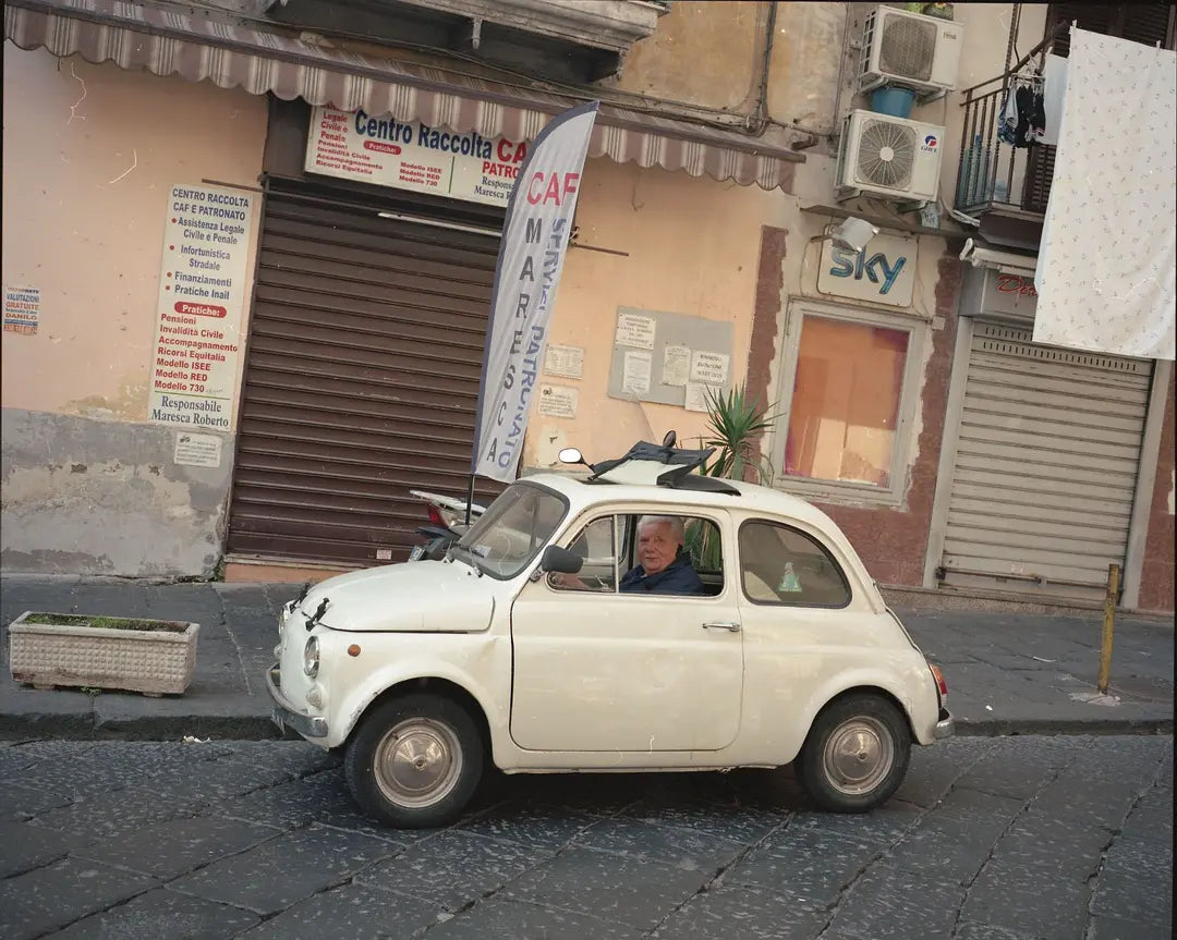 Small white car parked on a street with buildings